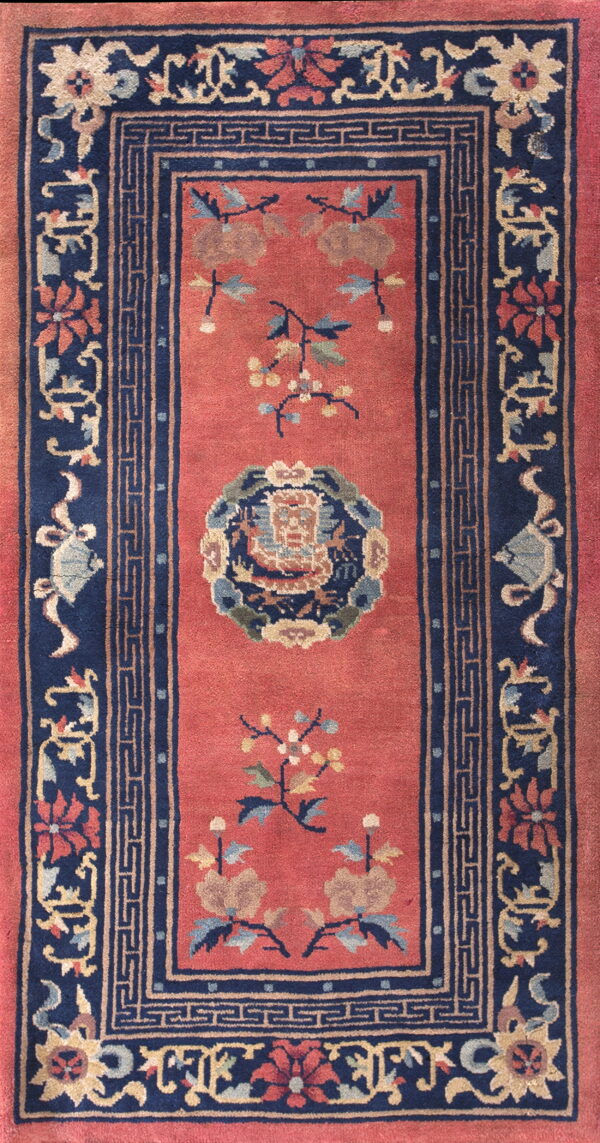 Rust-red runner rug with a navy border displaying ornate floral designs and a greek key pattern.