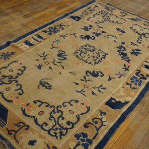 Angled view of a tan and blue patterned rug featuring coral flowers on distressed wood planks.