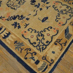 A beige rug with blue and coral floral patterns and borders rests on worn wood flooring.
