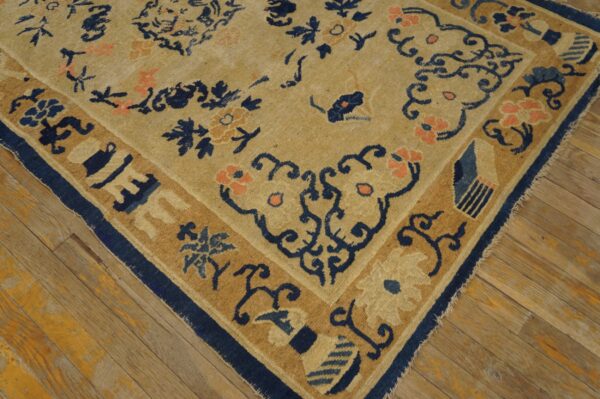 A beige rug with blue and coral floral patterns and borders rests on worn wood flooring.