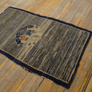 Low-pile rug featuring tan and dark blue vertical stripes and a central medallion on wood plank flooring.