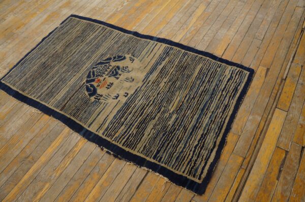 Low-pile rug featuring tan and dark blue vertical stripes and a central medallion on wood plank flooring.