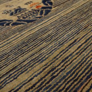 Detail shot of a rug showing ribbed dark blue and light tan stripes surrounding a stylized motif.