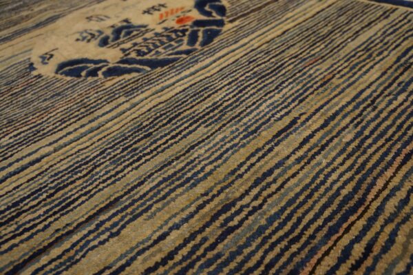 Detail shot of a rug showing ribbed dark blue and light tan stripes surrounding a stylized motif.