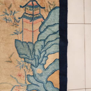 Beige rug with blue and pink pagoda and landscape patterns rests on white tile flooring.