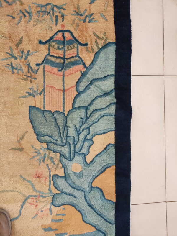 Beige rug with blue and pink pagoda and landscape patterns rests on white tile flooring.