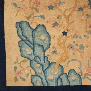 Beige high-pile rug detail showing stylized blue rocks, pink blossoms, and a navy border.