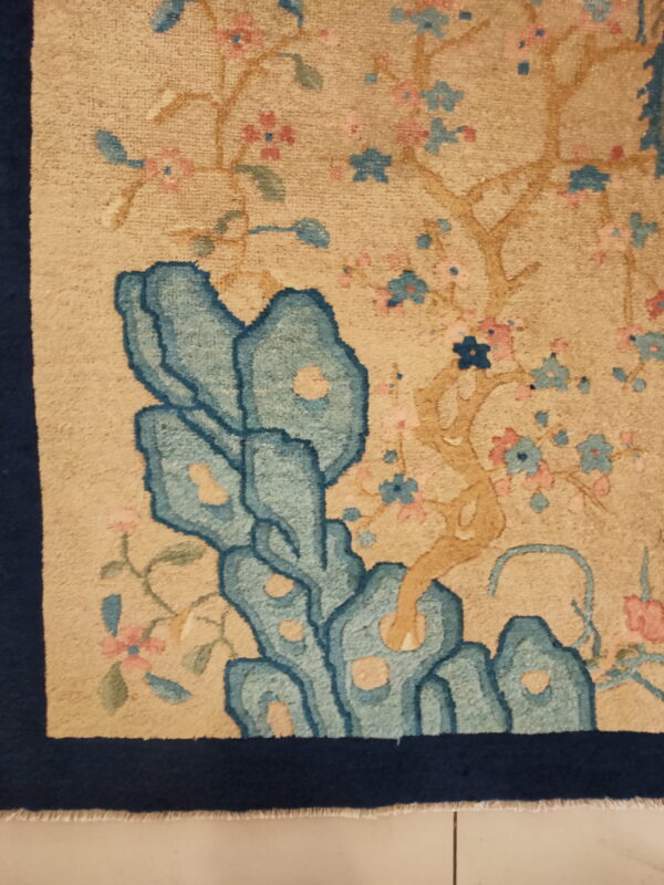Beige high-pile rug detail showing stylized blue rocks, pink blossoms, and a navy border.