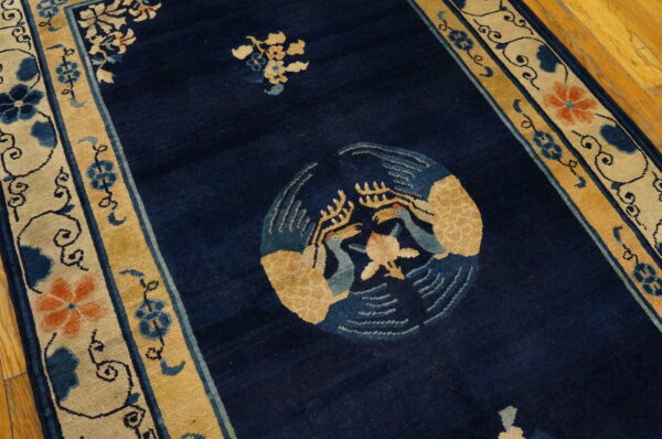 Navy blue rug featuring a golden bird motif and floral borders on light wood floor.