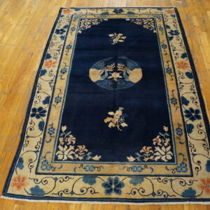 Navy blue rug with a central stylized bird medallion and wide beige floral border on wood floors.