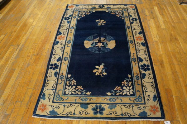 Navy blue rug with a central stylized bird medallion and wide beige floral border on wood floors.