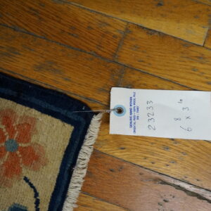 Beige rug corner featuring orange and blue flowers and a navy border on distressed hardwood flooring.