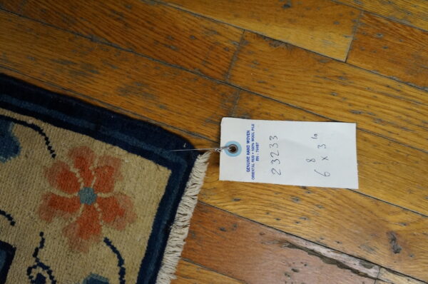Beige rug corner featuring orange and blue flowers and a navy border on distressed hardwood flooring.