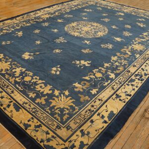 Oversized blue rug featuring a gold floral design and medallion resting on rustic wooden flooring.