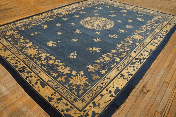 Oversized blue rug featuring a gold floral design and medallion resting on rustic wooden flooring.