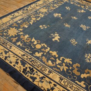 Blue rug with golden floral motifs and geometric borders displayed on worn wooden flooring.