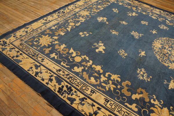 Blue rug with golden floral motifs and geometric borders displayed on worn wooden flooring.