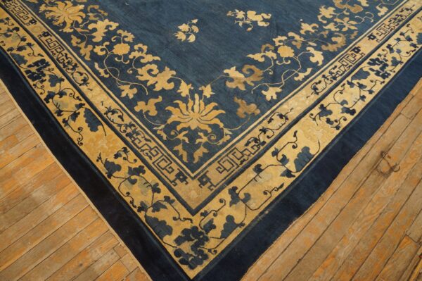 Deep blue rug with contrasting gold and blue floral border and corner motifs rests on wooden planks.