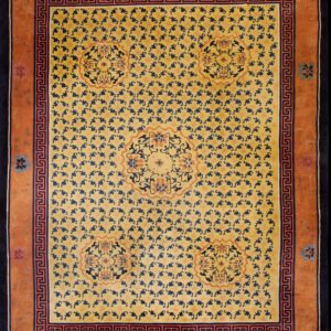 Yellow rug patterned with dark blue motifs, terracotta borders, and a Greek key design on wood flooring.
