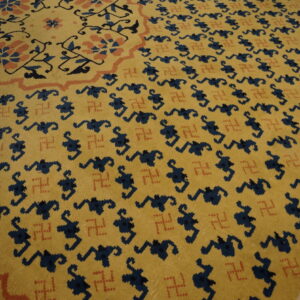 Mustard yellow rug featuring repeating navy stylized motifs, small rust-colored swastikas, and a geometric border.