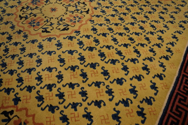 Mustard yellow rug featuring repeating navy stylized motifs, small rust-colored swastikas, and a geometric border.