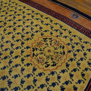 Yellow rug with navy symbols and rust accents, bordered by a Greek key pattern on hardwood floor.