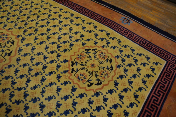 Yellow rug with navy symbols and rust accents, bordered by a greek key pattern on hardwood floor.