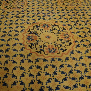Yellow rug with repeating dark blue patterns, an orange floral medallion, and a detailed Greek key border.