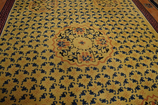 Yellow rug with repeating dark blue patterns, an orange floral medallion, and a detailed greek key border.