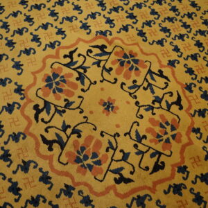 Gold rug with a navy and coral floral central medallion surrounded by repeating dark blue figures.