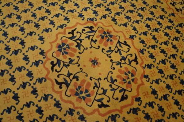 Gold rug with a navy and coral floral central medallion surrounded by repeating dark blue figures.