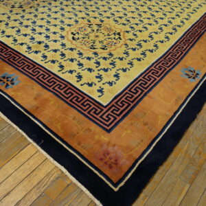 Gold rug with blue patterns, orange borders, and navy trim lies on worn light brown wood planks.