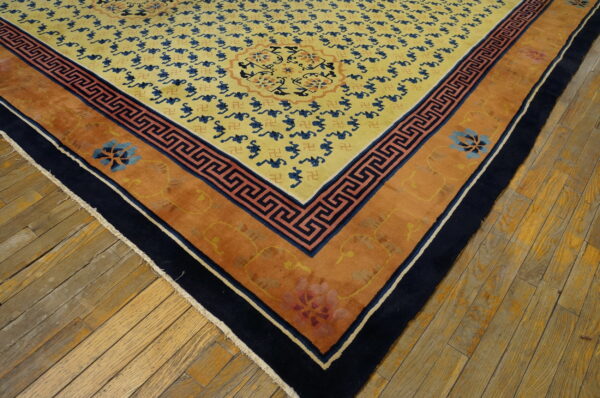 Gold rug with blue patterns, orange borders, and navy trim lies on worn light brown wood planks.