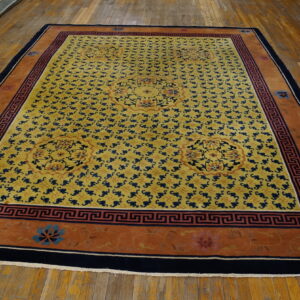 Yellow rug with navy blue repeat pattern, orange border, and central floral medallions on a wood floor.