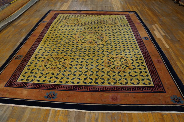 Yellow rug with navy blue repeat pattern, orange border, and central floral medallions on a wood floor.