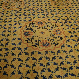 Low-pile yellow rug featuring repeating navy figures and large floral medallions bordered by orange and blue keys.