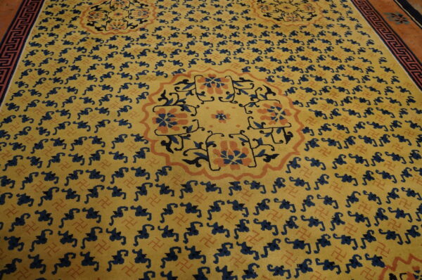 Low-pile yellow rug featuring repeating navy figures and large floral medallions bordered by orange and blue keys.