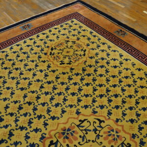 Gold rug featuring repeating blue and terracotta motifs, a geometric border, and a rust-colored edge on wood flooring.
