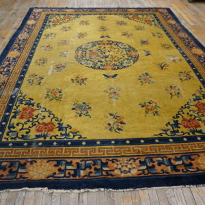 Yellow field rug with intricate floral and geometric navy blue borders rests on distressed wood planks.