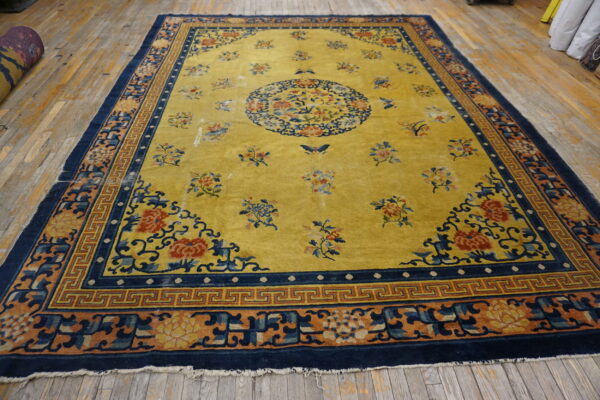 Yellow field rug with intricate floral and geometric navy blue borders rests on distressed wood planks.