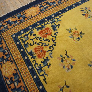 Yellow rug featuring red and blue floral designs, navy borders, laid on distressed wood flooring.