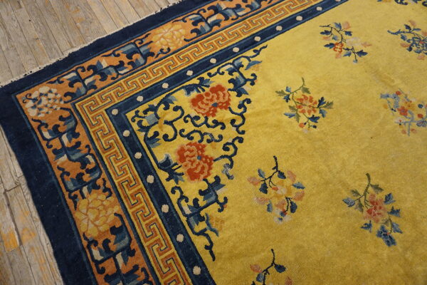 Yellow rug featuring red and blue floral designs, navy borders, laid on distressed wood flooring.