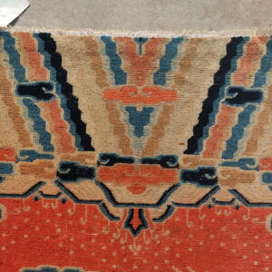 Fringed, low-pile rug section in orange, beige, blue, and black with abstract geometric patterns.