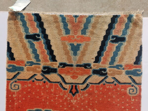 Fringed, low-pile rug section in orange, beige, blue, and black with abstract geometric patterns.