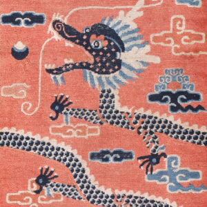Close-up of a rug featuring a navy blue dragon on a salmon pink field with light blue and ivory clouds.