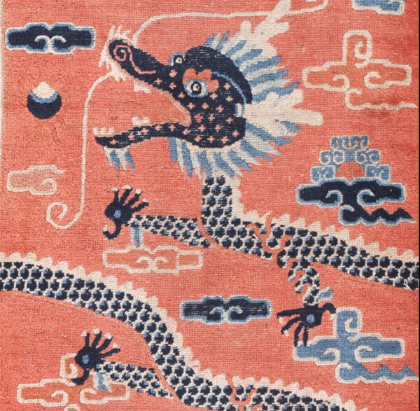 Close-up of a rug featuring a navy blue dragon on a salmon pink field with light blue and ivory clouds.