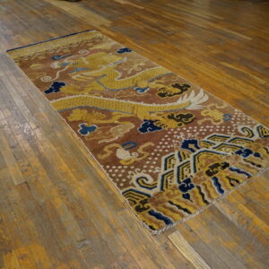 Brown and yellow runner rug with a traditional dragon motif displayed on aged wooden planks.
