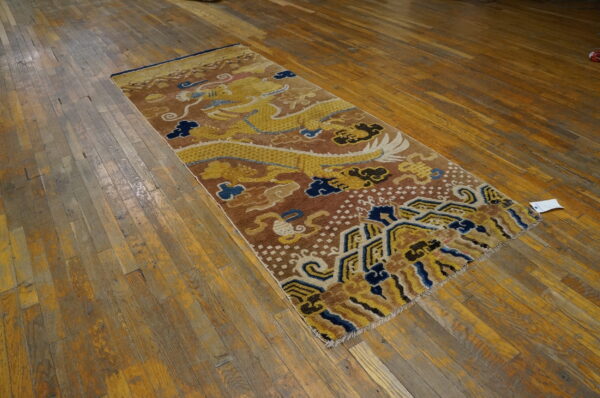 Brown and yellow runner rug with a traditional dragon motif displayed on aged wooden planks.