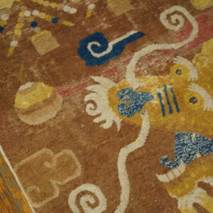 Stylized yellow and blue motifs on a textured brown rug, displayed on aged wood flooring.