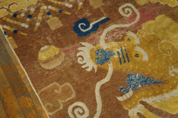 Stylized yellow and blue motifs on a textured brown rug, displayed on aged wood flooring.
